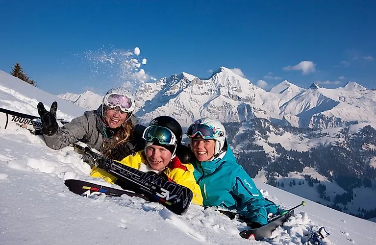 Tři lyžaři se smějí na sněhu se zasněženými horami v pozadí u Adelbodenu
