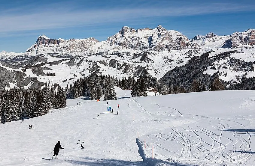 Des skieurs sur une piste enneigée avec les majestueuses Dolomites en arrière-plan, près de Corvara.