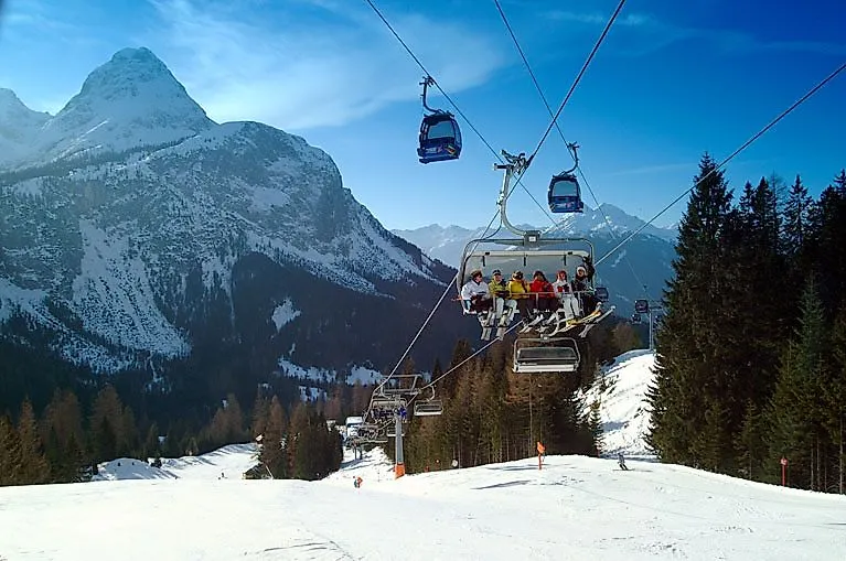 Lidé na sedačkové lanovce v Ehrwaldu s výhledem na zasněženou Zugspitze a okolní hory.
