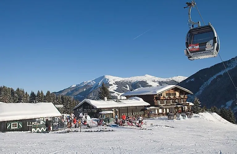 Zimní krajina s lanovkou a lyžaři před rustikální lyžařskou chatou v rakouském lyžařském středisku Leogang-Saalbach.