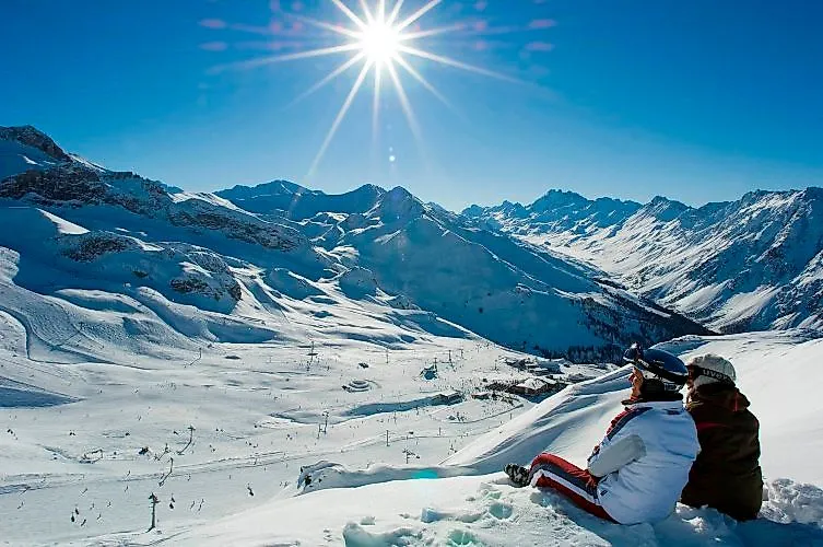 Zwei Skifahrer genießen das Panorama der schneebedeckten Silvretta Arena unter strahlender Wintersonne oberhalb von Ischgl.
