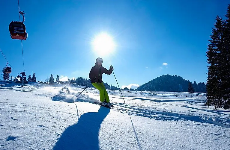 Skifahrer bei Sonnenschein auf einer verschneiten Piste in Oberstaufen mit Sessellift und Winterlandschaft in Oberstaufen