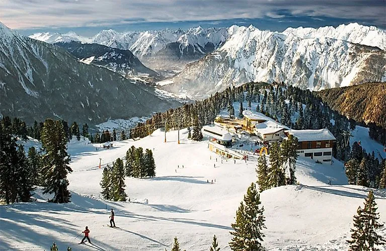 Lyžaři na sjezdovce u Oetzu s panoramatickým výhledem na zasněžené hory a lyžařskou oblast v Ötztalu.