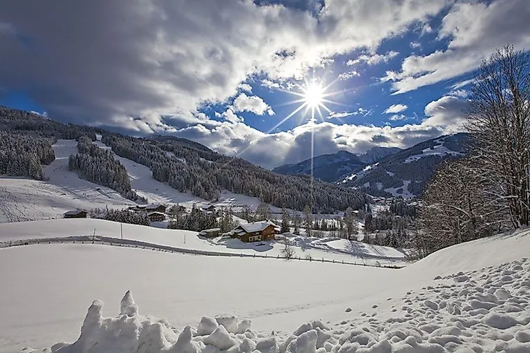 Snow-covered winter landscape in Wagrain with bright sunshine, ski slopes and rustic alpine huts in the background.