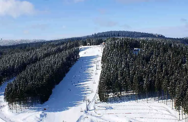 Wide ski slope in the snow-covered Winterberg ski area surrounded by dense forests in sunny winter weather
