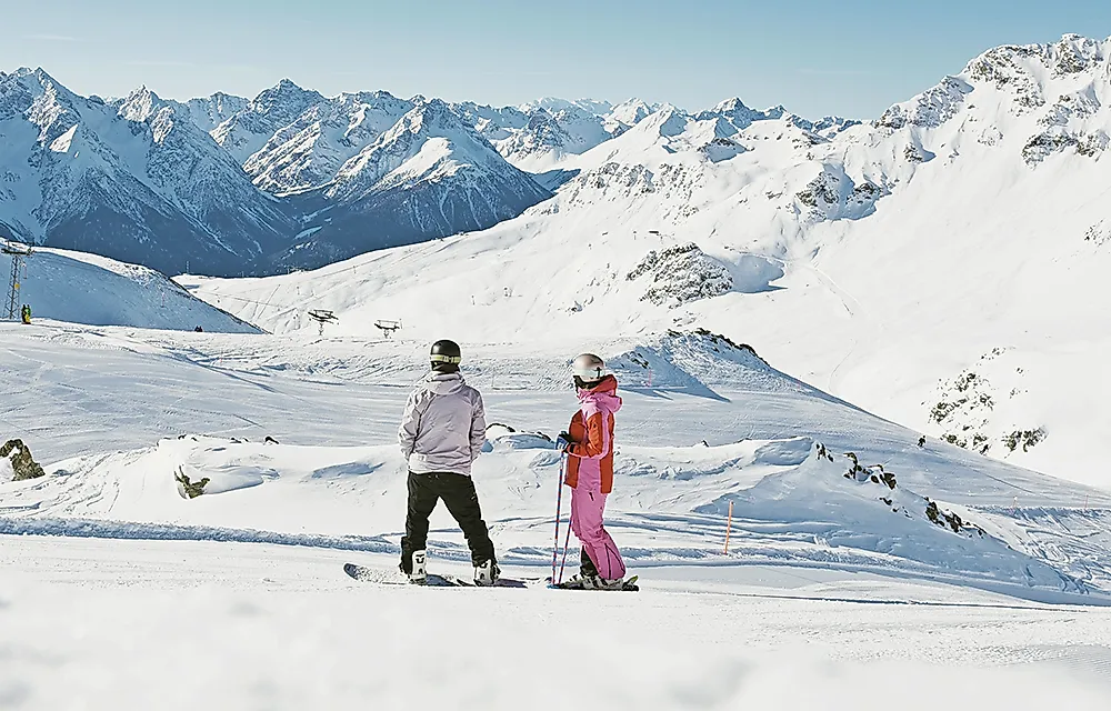 Zwei Skifahrer im Skigebiet Scuol vor verschneitem Bergpanorama