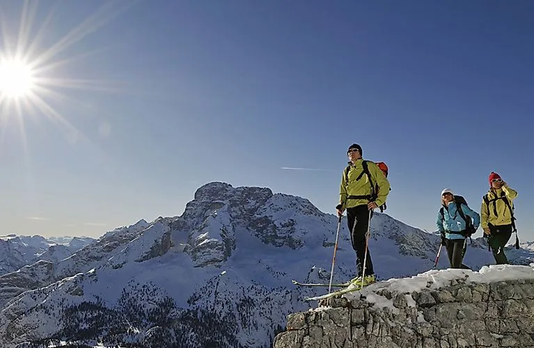 Traja skialpinisti v Seste so zasneženými Dolomitmi v pozadí na slnku