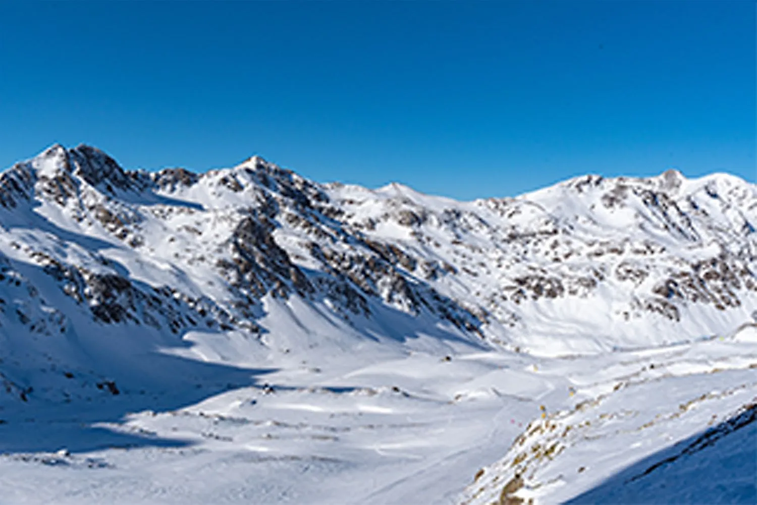 Schneebedeckte Gipfel und Skipisten im Skigebiet Ordino-Arcalís in Andorra unter blauem Himmel