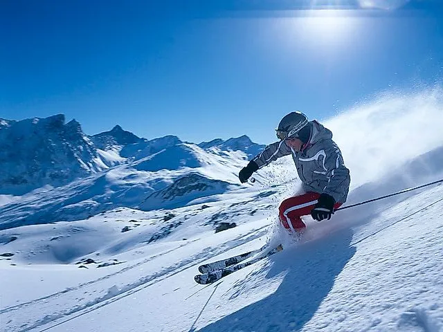 Esquiadores bajando por una pista nevada en Savognin con un impresionante telón de fondo alpino bajo un cielo azul brillante.