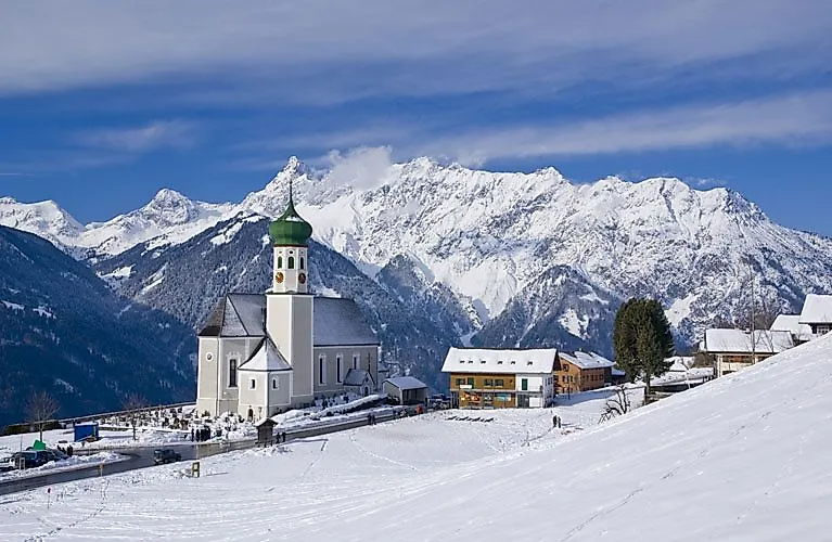 Snow-covered village with church and Alpine panorama in Vorarlberg in winter