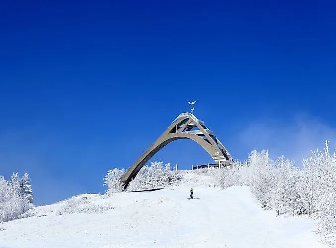 Snow-covered St. Georg ski jump in Winterberg with skiers and a deep blue sky on a clear winter's day