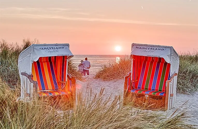 Deux chaises de plage colorées dans le Wangerland avec vue sur le coucher de soleil à la mer du Nord, couple se promenant sur la plage