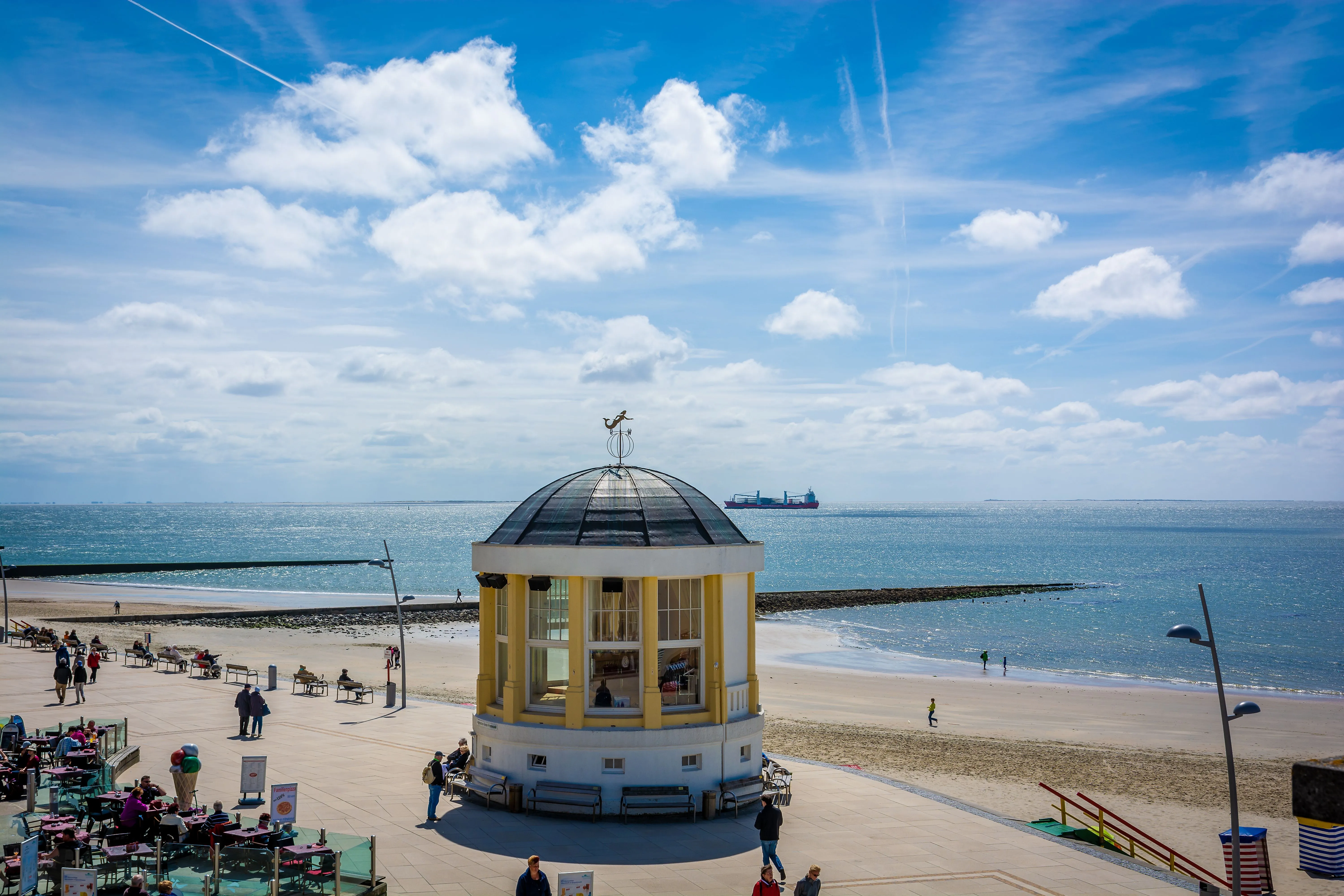 Borkum beach promenade with pavilion, sea view and strollers in the sunshine.