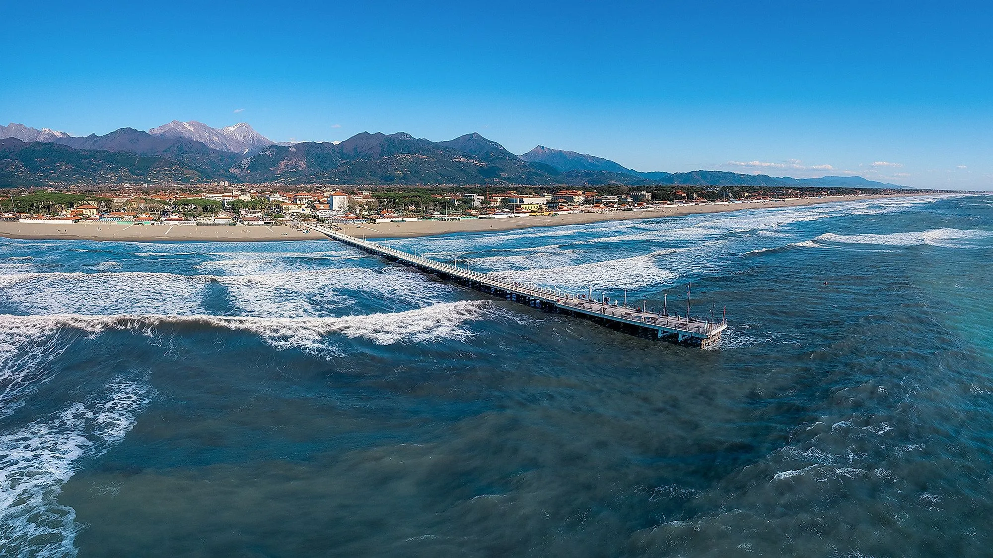 Beach and promenade of Forte dei Marmi in Tuscany with a view of the sea and the Apuan Alps in the background.