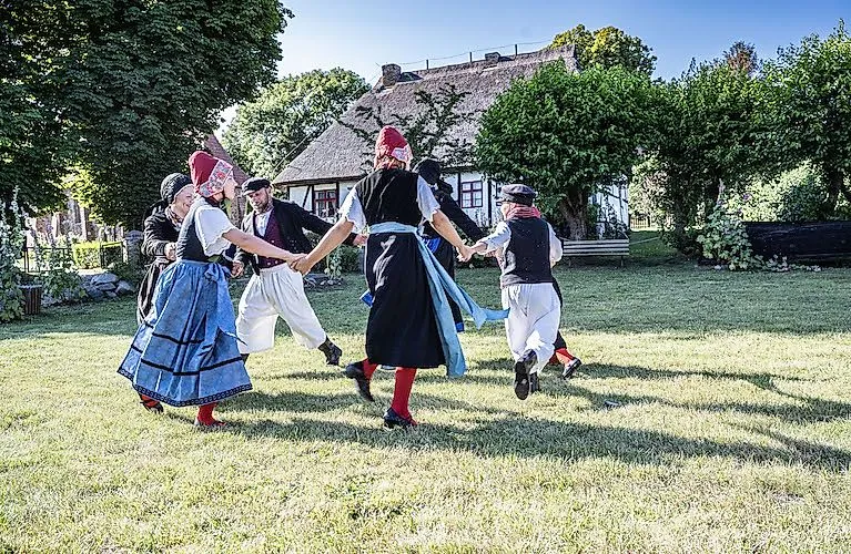 Ľudia v tradičných krojoch tancujú pred slameným domom v Mönchgute na ostrove Rujana.