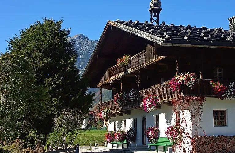 Tradizionale cascina tirolese con decorazioni floreali e montagne sullo sfondo, in una giornata di sole.