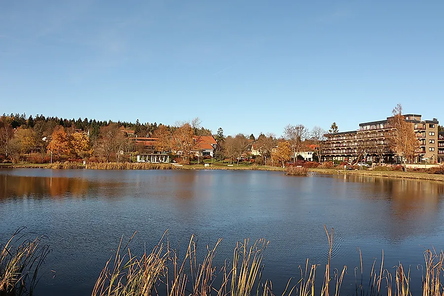 Kranicher Teich in Hahnenklee im Harz mit herbstlichen Bäumen und Häusern am Ufer unter blauem Himmel