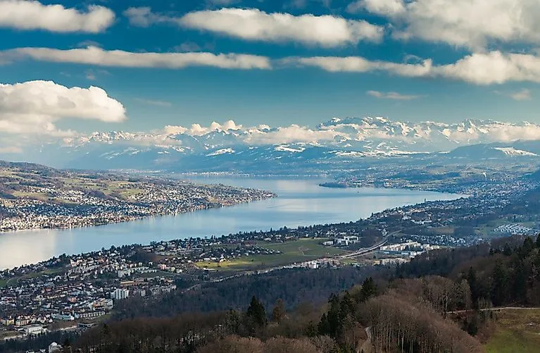 Far-reaching view over Lake Zurich with adjacent cityscape and snow-capped Alps in the background.