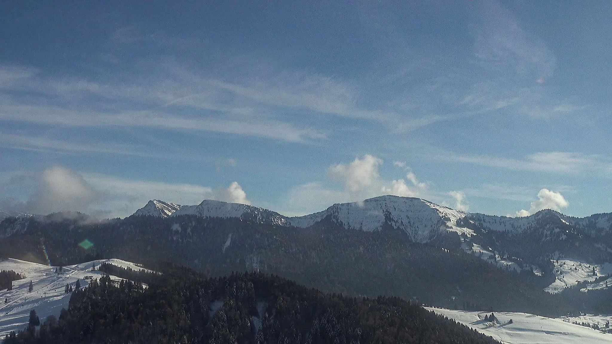 Winterpanorama in Oberstaufen im Allgäu mit verschneiten Berggipfeln, Skipisten und bewaldeten Hängen