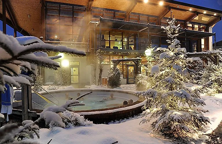 Relaxující hosté v teplém venkovním bazénu Obermain Therme, obklopeni zasněženou zimní krajinou.