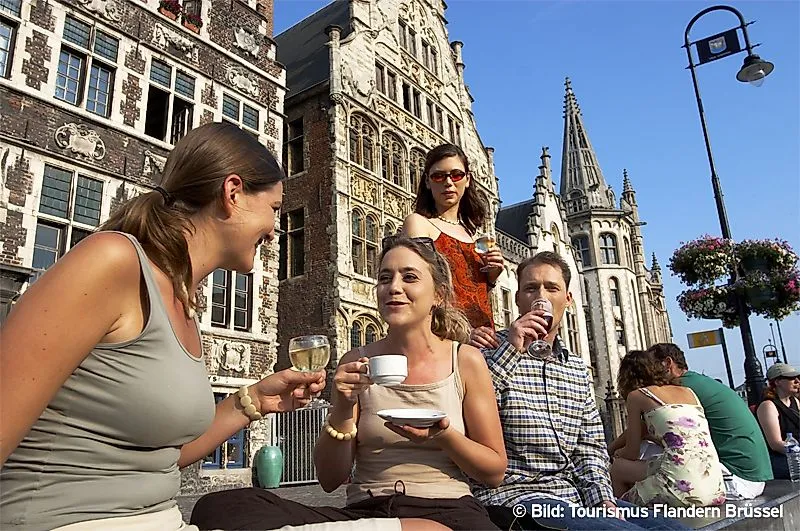 Lidé si vychutnávají nápoje před historickými budovami v belgickém Gentu