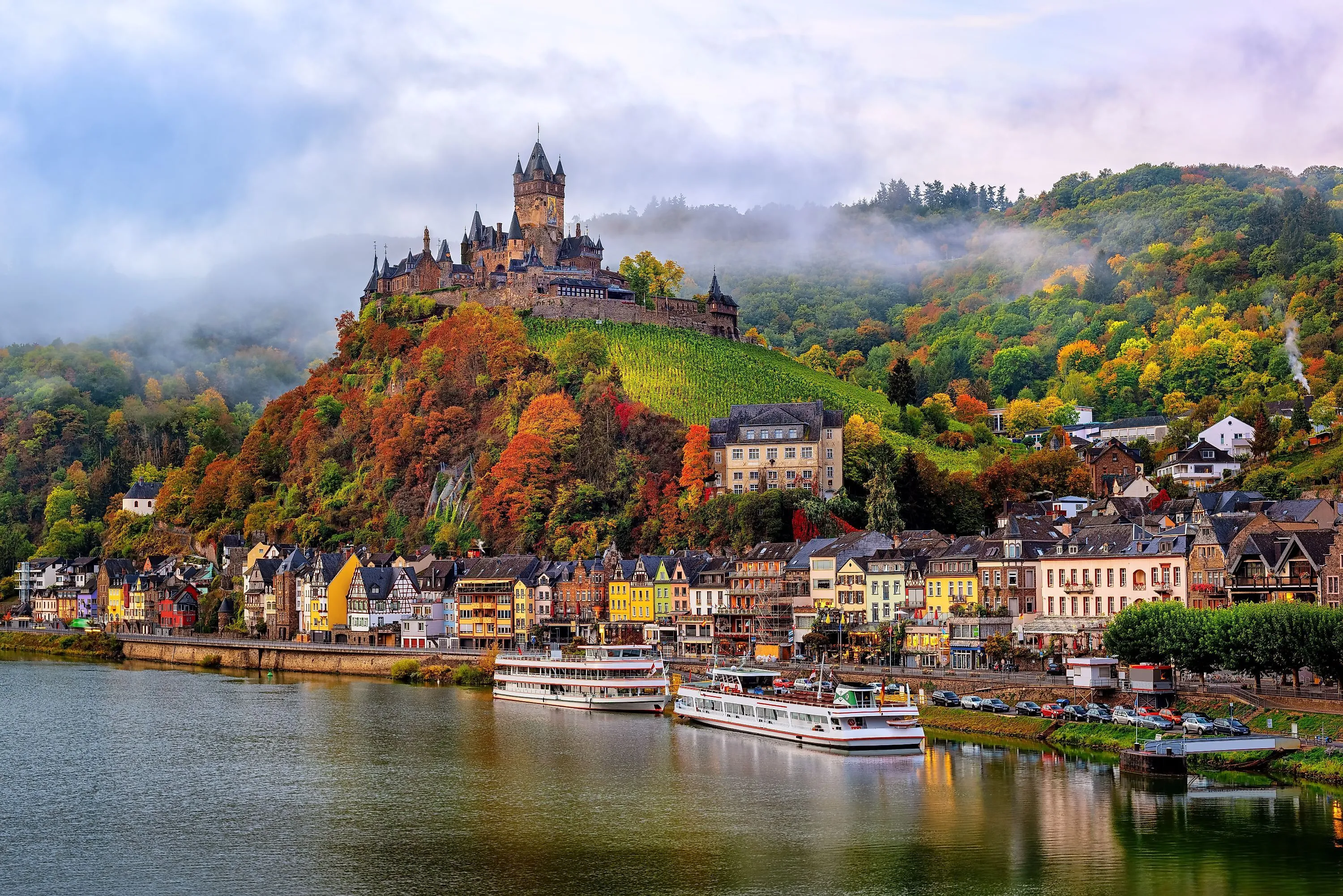 Reichsburg Cochem op een groene heuvel boven de Moezel met kleurrijke huizen en schepen