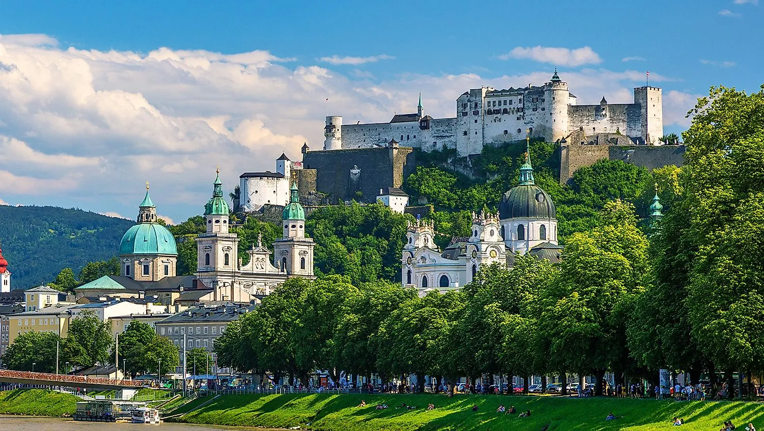 Panoramatický pohľad na historické centrum Salzburgu s kupolami barokových kostolov a impozantnou pevnosťou Hohensalzburg na kopci v pozadí.