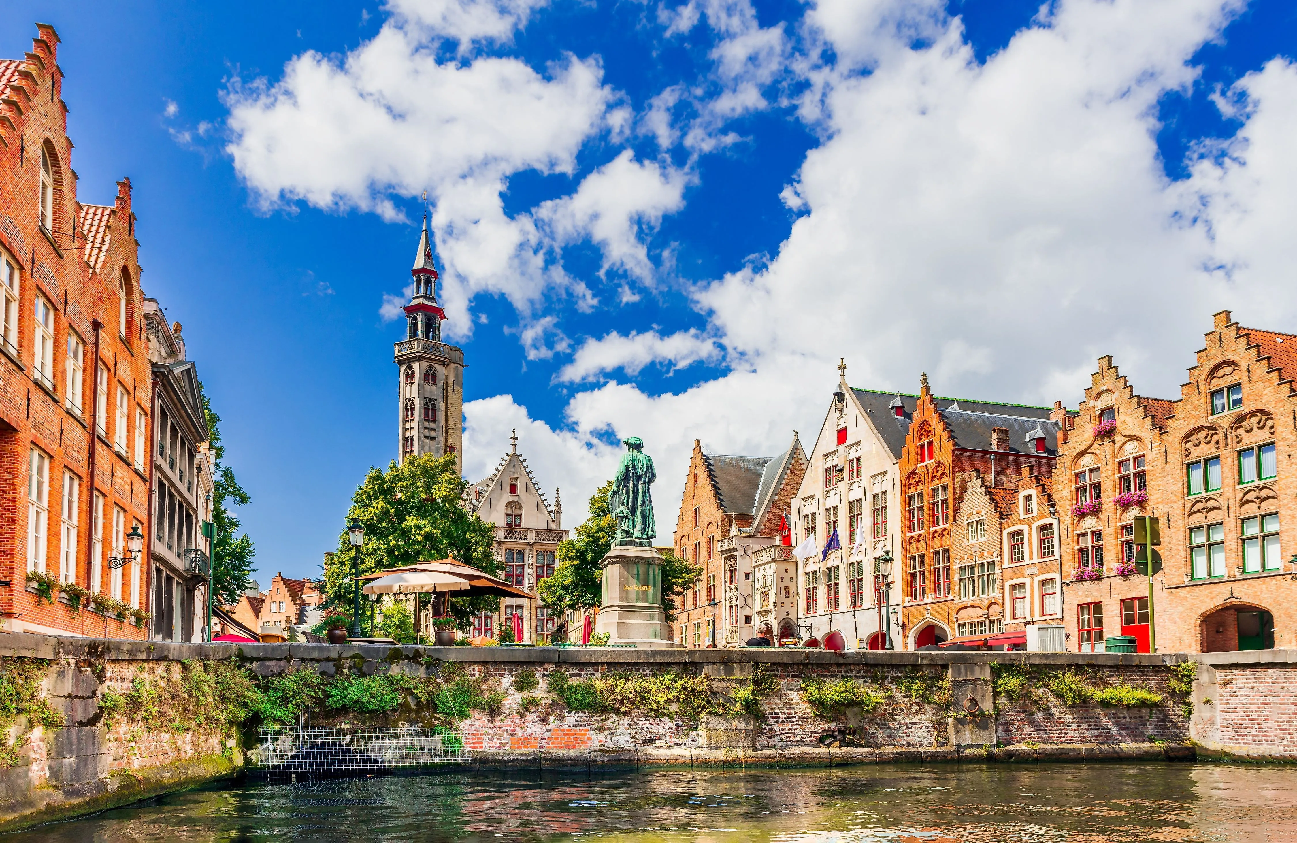 Canal in Bruges with historic gabled houses and Jan Breydel statue in the sunshine