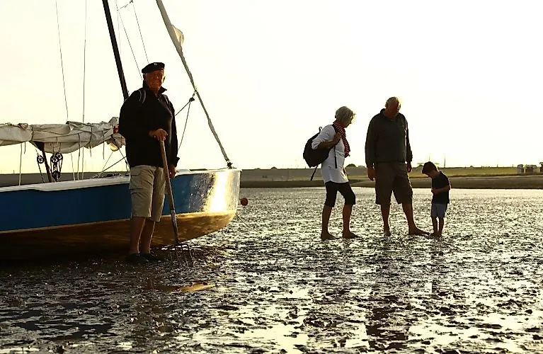Menschen bei Ebbe auf einer Wattwanderung im Meer von Langeoog neben einem Segelboot im Abendlicht