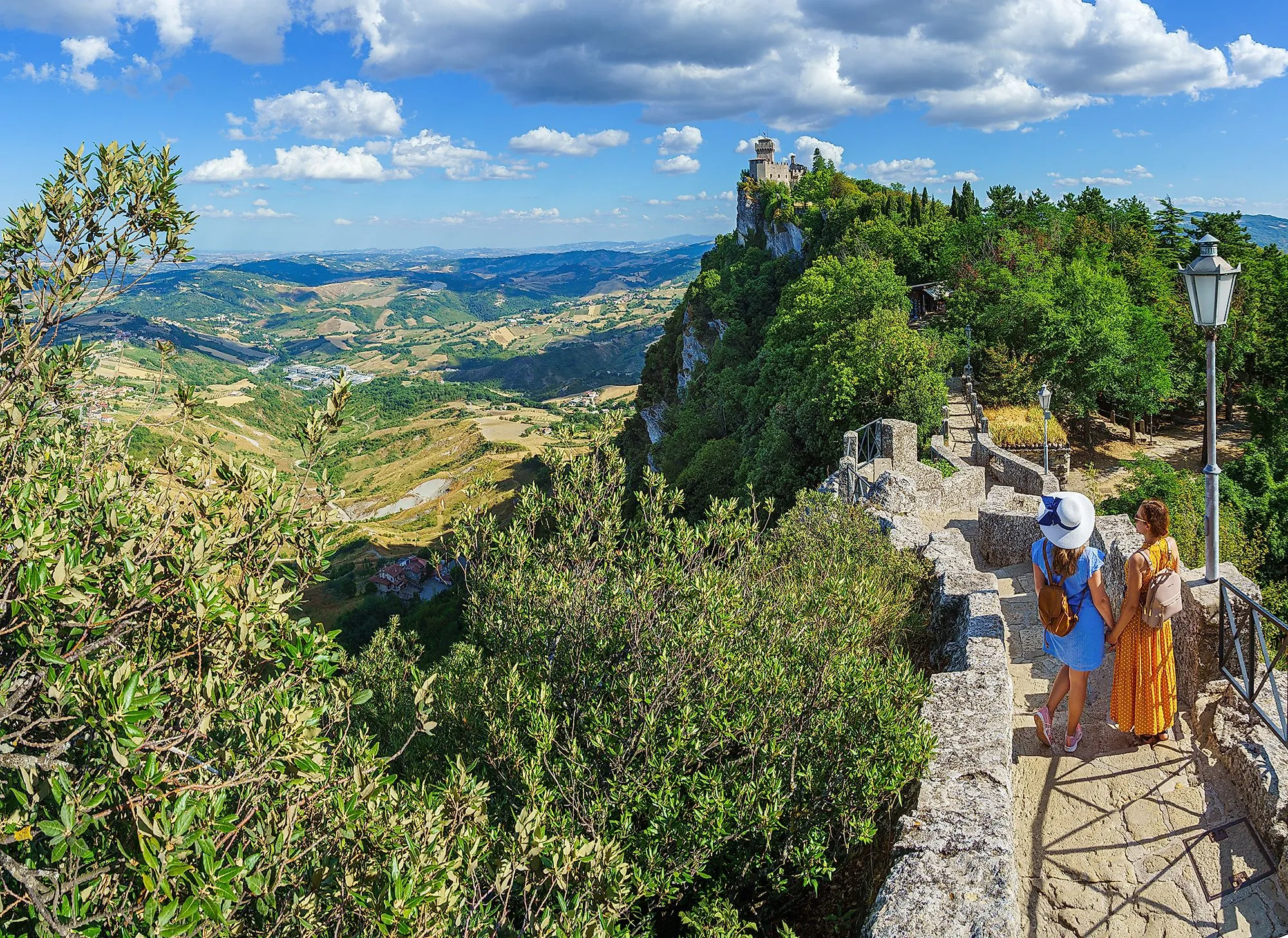 Dos mujeres en una ruta de senderismo en San Marino con vistas a la fortaleza de Cesta y las colinas circundantes.