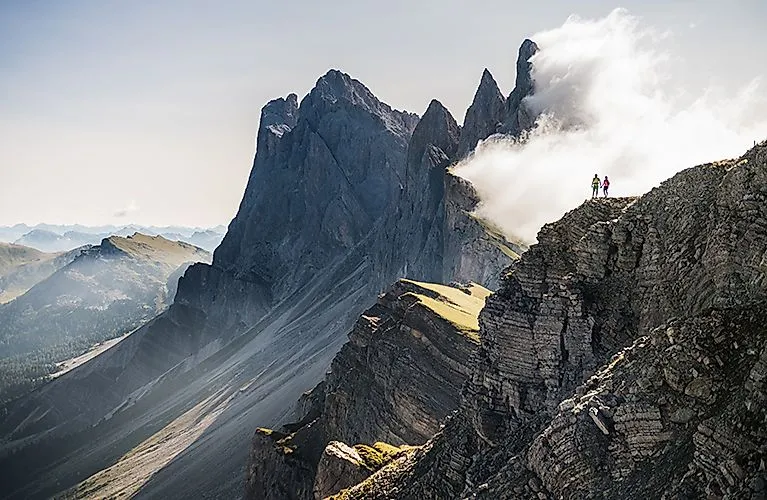 Two hikers on a steep Dolomite ridge surrounded by clouds and rocks