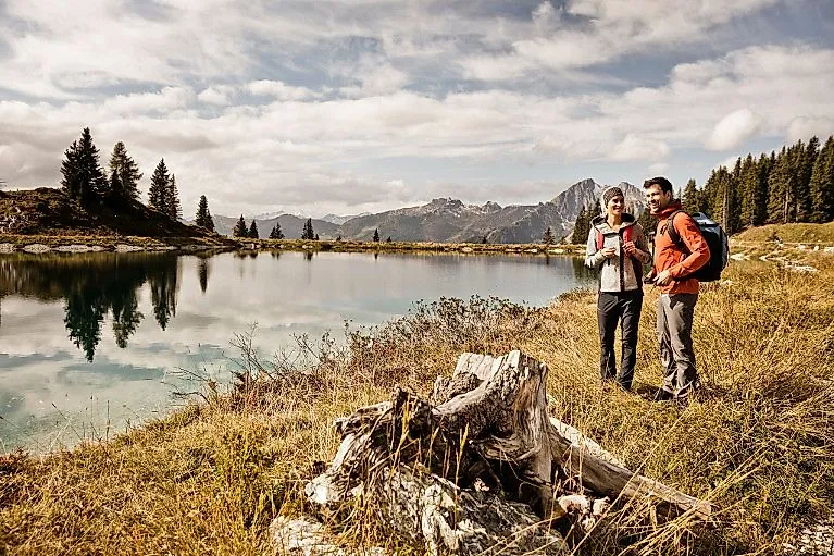 Dva turisté si užívají pohled na průzračné horské jezero ve vysokohorské krajině za podzimního počasí v St. Johann im Pongau.