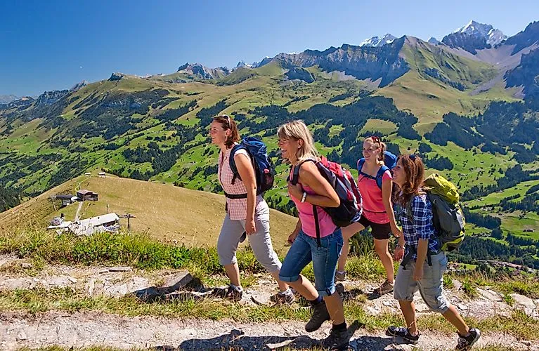 Skupina turistů na slunné horské stezce s výhledem na zelené údolí u Adelbodenu ve Švýcarsku