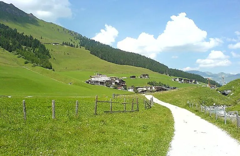 Wanderweg mit Blick auf das idyllische Dorf Hintertux in Tirol, eingebettet in grüne Almwiesen und sanfte Berghänge unter blauem Himmel.