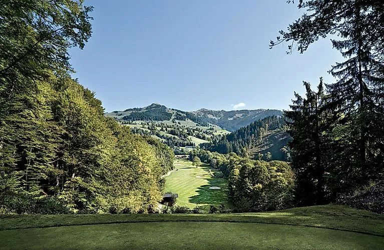 Pohled na udržované údolí s golfovým hřištěm, které je lemováno hustými zelenými lesy a kopci v oblasti Kitzbühelu.
