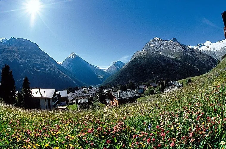 Un prato fiorito sullo sfondo alpino e un villaggio nella Valle di Saas con il sole dell'estate.