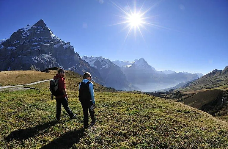 Zwei Wanderer mit Blick auf das Bergpanorama bei Wengen unter strahlender Sonne.