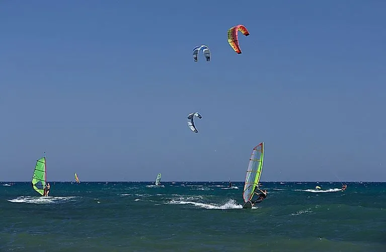 Surfaři a kitesurfaři na moři u Cambrils za silného větru - oblíbené místo pro vodní sporty na pobřeží Costa Daurada