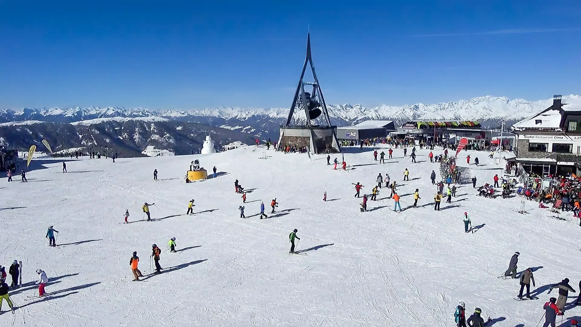 Skifahrer am Kronplatz-Gipfel mit Friedensglocke Concordia 2000 und verschneitem Bergpanorama