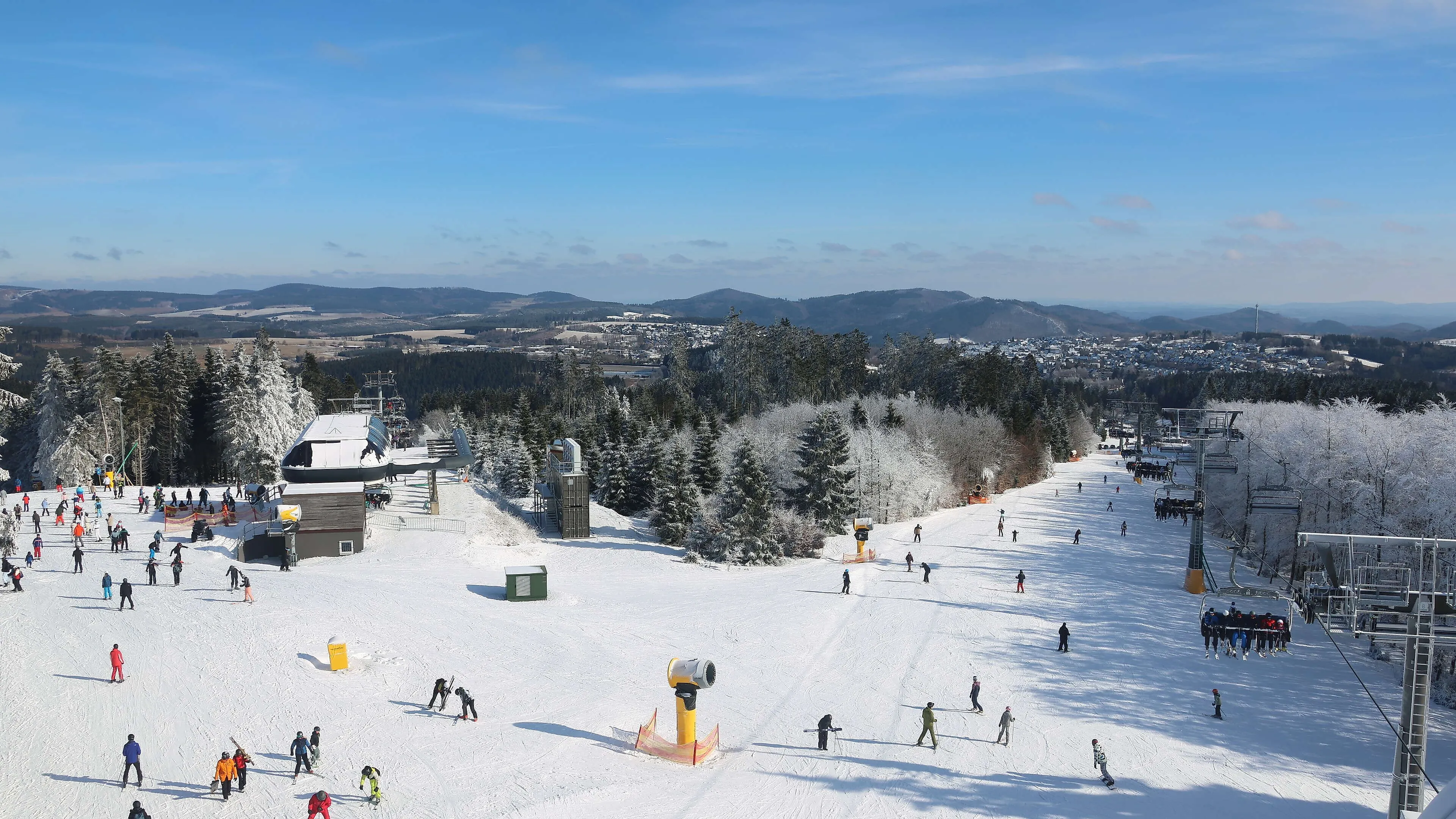Skiers on the snow-covered slope at Brembergkopf in Winterberg, with a chairlift and a wintry forest landscape