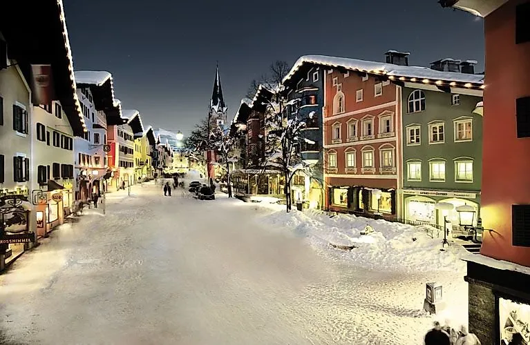 Atmosfera invernale serale nel centro storico di Kitzbühel con le facciate delle case illuminate, le strade innevate e le persone che passeggiano per la città in inverno.