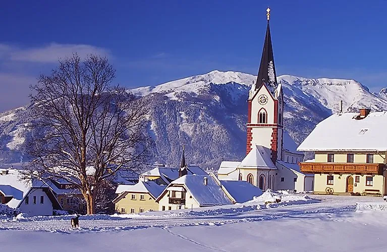 Winter landscape in Mariapfarr with snow-covered houses and the famous church against the mountain backdrop in Salzburg's Lungau region.