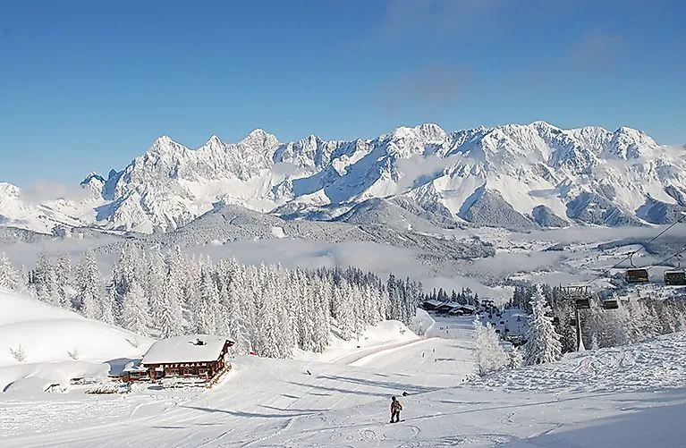 Besneeuwd winterlandschap op de Reiteralm met skiërs op de piste en uitzicht op het Dachsteinmassief op de achtergrond.