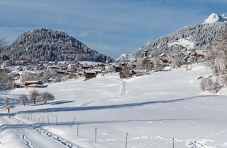 Paysage hivernal de Brigels avec des collines enneigées, des maisons et des montagnes environnantes.