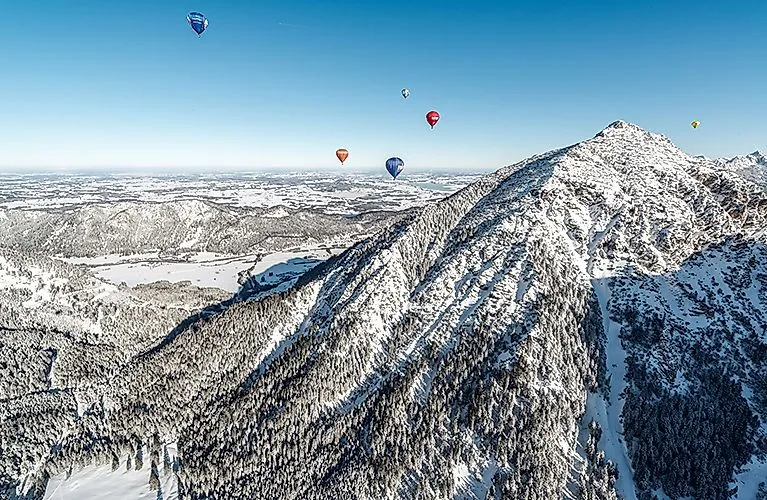 Besneeuwd berglandschap in het Tannheimer Tal met kleurrijke heteluchtballonnen in de lucht bij Grän in de winter.