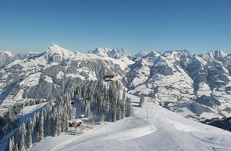 Paesaggio montano innevato con cime imponenti e una cresta boscosa; una baita troneggia sull'Hahnenkamm al di sopra della linea degli alberi.