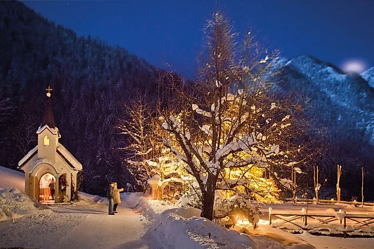 Atmosférický zimní záběr osvětlené kaple s vánočním stromem na sněhu v noci v St. Johann im Pongau.