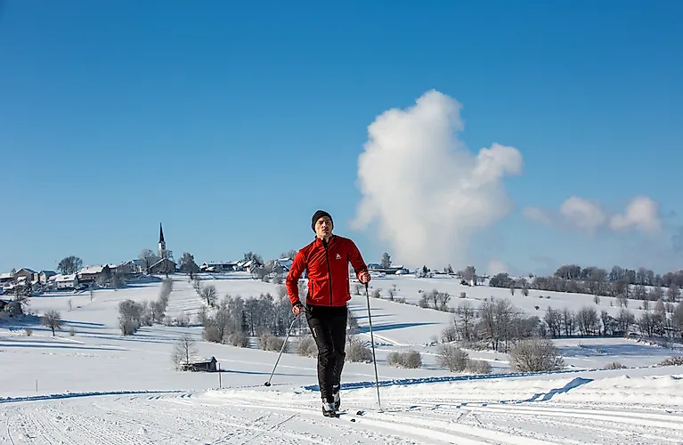 Cross-country skiers on a snow-covered trail near Freyung, with a winter landscape and a church tower in the background