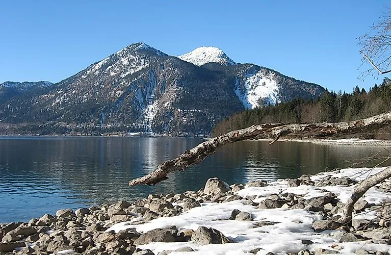 Winterlandschaft am Kochelsee mit verschneiten Bergen und vereisten Uferbereichen.