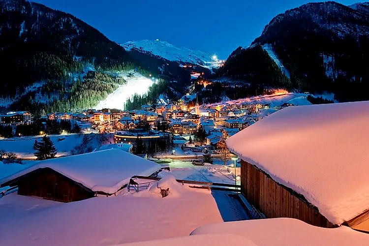 Winterlicher Abendblick auf das beleuchtete Ischgl mit glitzernden Schneedächern, Pisten und stimmungsvoller Bergkulisse.